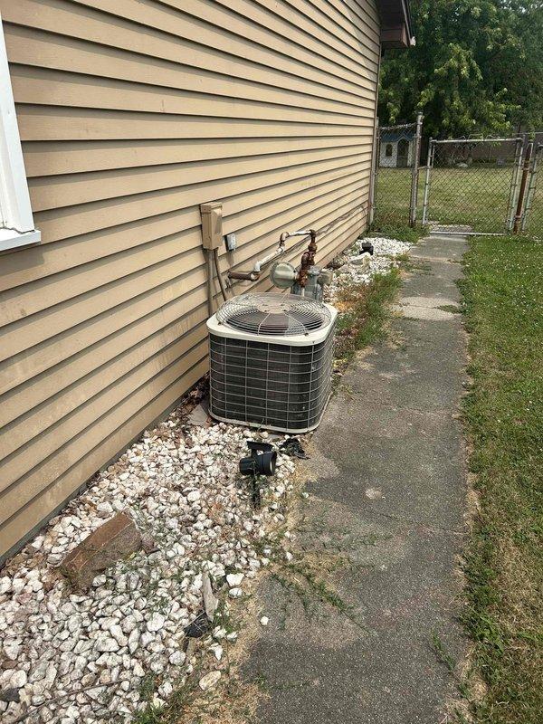 Conducted comprehensive site evaluation of existing residential HVAC system under tech lead supervision. Documented current air conditioning condenser unit installation, including equipment placement on concrete pad with white decorative stone surround for proper drainage. Assessed exterior-mounted electrical components, conduit routing, and junction box configuration along vinyl siding. Evaluated copper refrigerant line runs from condenser to building penetration point. Photographed equipment positioning relative to property boundaries, walkways, and utility access points to determine optimal replacement unit placement and clearance requirements. Prepared detailed estimate for complete system replacement based on existing installation conditions and site constraints.