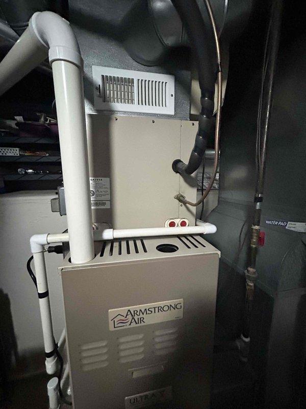 # HVAC System Replacement Estimate

Conducted comprehensive evaluation of residential HVAC system with all equipment approximately 24 years old. Assessed outdoor air conditioning unit, indoor furnace system, and water heater for replacement recommendations.

## Equipment Assessed

**Outdoor Unit:**
Inspected existing beige/tan cylindrical condenser unit with top-mounted fan assembly positioned on exterior pad. Evaluated electrical disconnect box, conduit routing, and refrigerant line connections. Unit mounted on level surface against building exterior with proper clearances maintained.

**Indoor Equipment:**
Examined Armstrong Air furnace installation in mechanical room with integrated blower assembly. Assessed white PVC exhaust/intake ventilation piping configuration extending from furnace cabinet. Evaluated copper refrigerant line routing along wall and electrical connections to system components. Reviewed water heater condition positioned adjacent to HVAC equipment.

## System Evalu