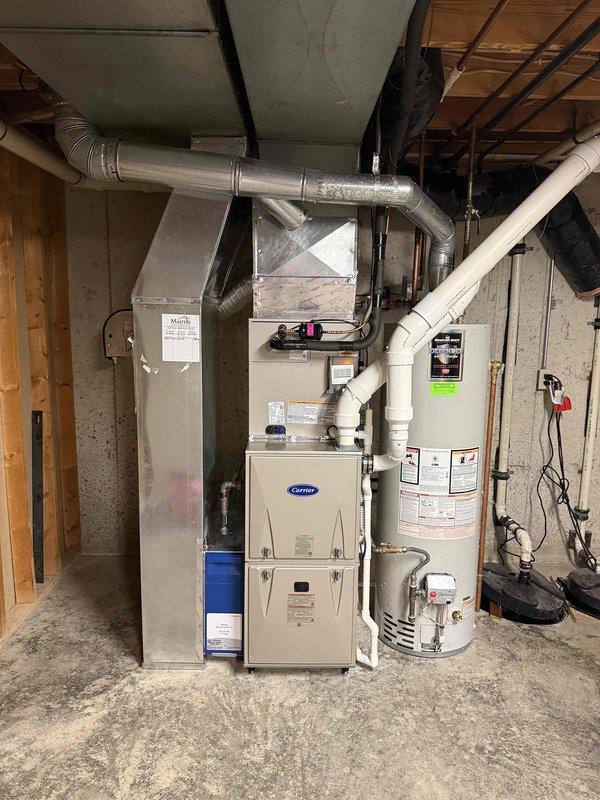Completed full HVAC system installation in basement mechanical room, including Carrier furnace unit with integrated ductwork distribution system, air handler with humidifier component, and outdoor condensing unit. Installed white PVC venting system routed through ceiling joists, established metallic supply and return ductwork connections, and integrated copper refrigerant line set between indoor and outdoor equipment. Configured Honeywell Home programmable thermostat (model TH6210U2001) with battery backup and mounted control wiring throughout system for proper communication between all components, ensuring complete heating and cooling functionality with proper airflow distribution and system controls operational.