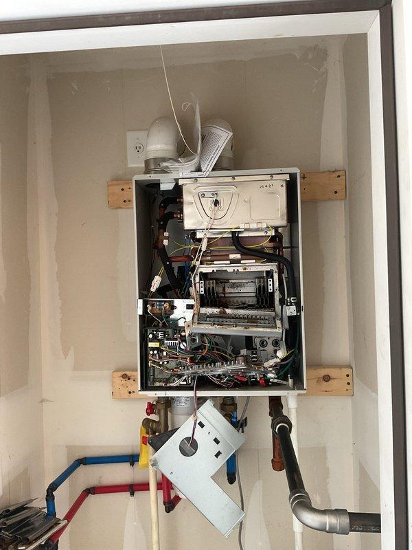 Responded to service call for leaking tankless water heater unit. Upon arrival, inspected wall-mounted tankless water heater system installed in recessed cabinet space. Removed front access panel to expose internal components including circuit boards, wiring harnesses, heat exchanger elements, and control mechanisms. Identified source of leak and assessed condition of unit, which is an AT-H3-DV-SCM-N model natural gas tankless water heater with 15,000-199,000 BTU capacity. Examined all water connections, including inlet and outlet piping, pressure relief valve, and condensate drain system. Inspected venting system including metal elbow joint and flexible vent pipe for proper installation and potential moisture intrusion points. Evaluated electrical connections and control panel functionality. Documented unit specifications and current installation configuration with detailed photographs for service records and potential warranty claim or replacement recommendations.