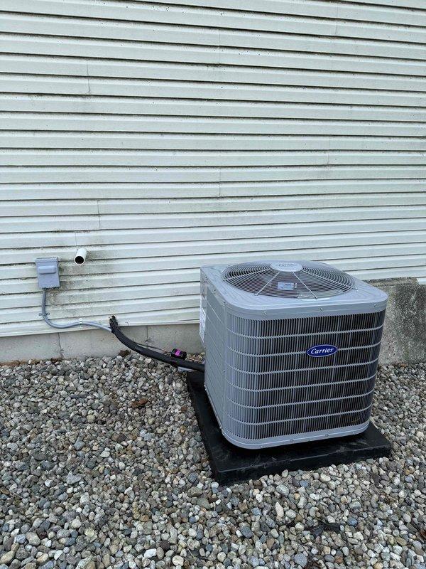 Completed installation of Carrier 26SPA636W003 air conditioning condenser unit and CVAVA4217XMA evaporator coil system. Positioned outdoor condenser on rubber pad with gravel base against building exterior, installed electrical disconnect box with proper conduit and wiring, and connected refrigerant lines between outdoor and indoor units. Indoor evaporator coil integrated with existing furnace system, with PVC condensate drainage piping installed and all ductwork connections properly sealed and secured.