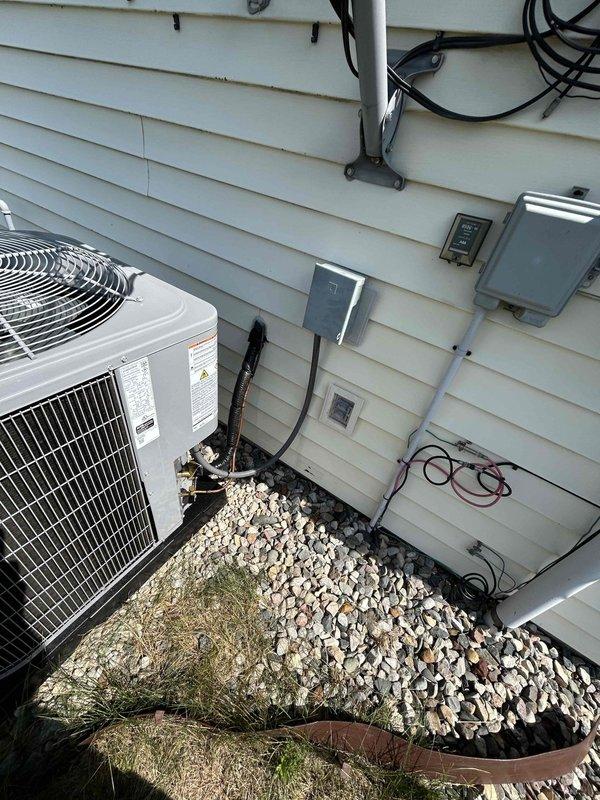 Conducted on-site evaluation for complete HVAC system replacement of 23-year-old existing equipment. Assessed current wall-mounted heating unit in garage and exterior air conditioning condenser unit. Documented existing system configuration including electrical connections, conduit routing, PVC condensate drainage, and equipment placement. Evaluated installation requirements for new equipment replacement including electrical service capacity, refrigerant line routing, and proper clearances for outdoor condenser unit positioned on gravel pad with landscape edging.
