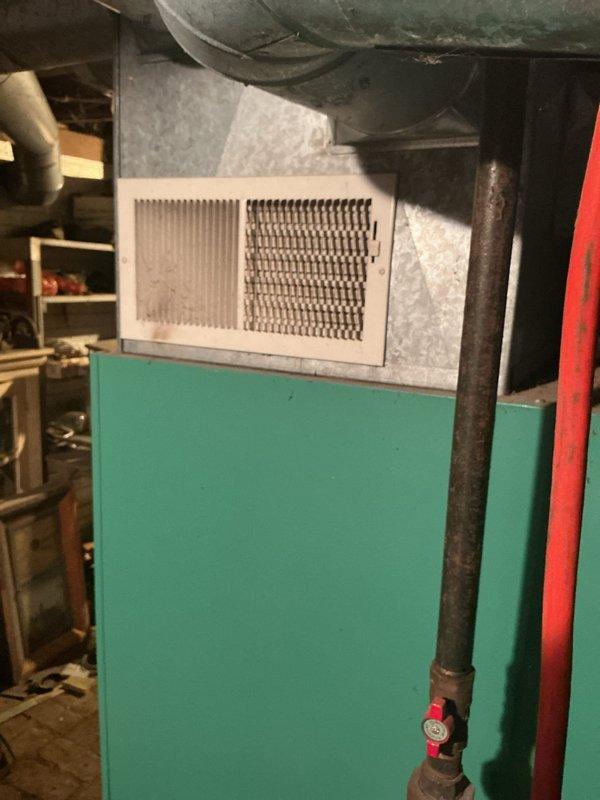 Conducted on-site assessment of 32-year-old Williamson propane gas furnace system located in basement utility area. Unit showing significant age-related wear and approaching end of serviceable life. Documented existing equipment configuration including green cabinet heating unit, PVC venting system, metallic ductwork with visible condensation, and basement installation environment. Photographed current system setup, floor register placement, gas piping with shut-off valve, and surrounding mechanical space conditions. Provided comprehensive replacement estimate for new propane furnace system to address aging equipment concerns and ensure continued reliable heating operation.