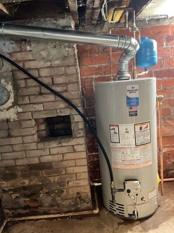 Installed new Bradford White natural gas tanked water heater in basement utility room, replacing existing unit. Brought installation up to current plumbing code requirements and addressed safety concerns with previous setup. Work included proper venting installation with metal exhaust piping, connection of copper supply lines, and integration of existing water treatment components. Two-person crew required for safe removal of old unit and positioning of new equipment. All connections tested and verified operational upon completion.