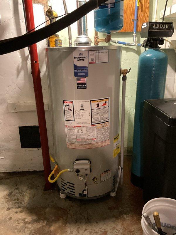Responded to service call for leaking tanked gas water heater in basement utility area. Upon arrival, confirmed customer had shut off water supply to the unit to prevent further water damage. Performed thorough inspection of Bradford White 48-gallon natural gas water heater (Model CB56697051, 40,000 BTU input rating). Assessed unit condition, examined all plumbing connections, gas lines, and surrounding water treatment system. Documented existing installation configuration including red supply piping, ventilation ductwork, and adjacent blue water filtration tank. Photographed water heater specifications, manufacturer labels, and overall equipment setup for service records. Identified leak source and evaluated repair versus replacement options based on unit age and condition. Provided technical recommendations to homeowner for resolution of the leak issue.