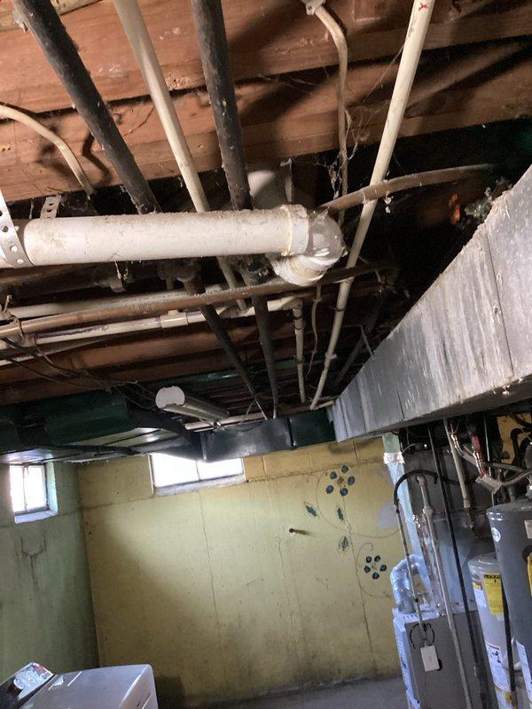 Responded to service call regarding unusual odor at rental property. Conducted thorough inspection of basement utility area and plumbing system to identify source of smell. Upon examination, discovered severely corroded vertical water supply pipe with extensive rust and surface degradation. Inspected all exposed plumbing including PVC drainage lines, vent pipes, and supply lines running through basement ceiling joists. Photographed corroded pipe and overall plumbing configuration for documentation. Confirmed odor was not sewer gas but likely related to deteriorated metal piping and potential moisture issues in the basement area. Recommended replacement of corroded pipe to prevent future leaks and eliminate odor source.