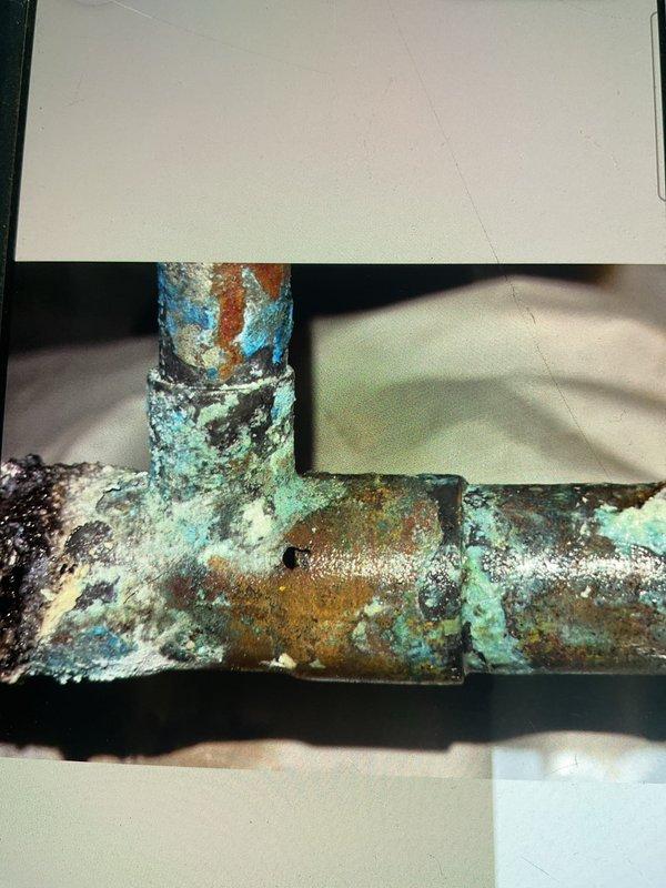 Responded to emergency call for burst pipe in crawlspace under kitchen area. Upon inspection, identified a failed 3/4x3/4x1/2 copper tee fitting that had split and was actively spraying water against the subfloor above. Instructed homeowner to shut off main water supply immediately to prevent further damage. Assessed extensive water damage throughout crawlspace including saturated ductwork hanging down, wet electrical wiring, lighting fixtures, and fans creating potential safety hazards. Coordinated with water mitigation company to schedule emergency water extraction and drying services. Documented severe corrosion and deterioration of copper piping system with heavy turquoise and blue-green patina buildup indicating long-term moisture exposure. Job placed on hold pending completion of water removal and drying to allow safe access for permanent pipe repair and replacement of damaged tee fitting.