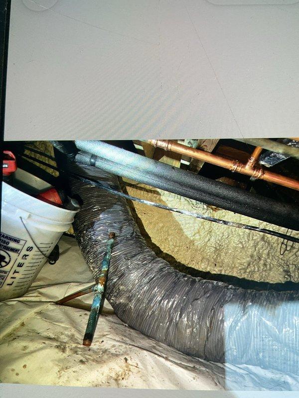 Responded to emergency call for burst pipe in crawlspace under kitchen area. Upon inspection, identified a failed 3/4x3/4x1/2 copper tee fitting that had split and was actively spraying water against the subfloor above. Instructed homeowner to shut off main water supply immediately to prevent further damage. Assessed extensive water damage throughout crawlspace including saturated ductwork hanging down, wet electrical wiring, lighting fixtures, and fans creating potential safety hazards. Coordinated with water mitigation company to schedule emergency water extraction and drying services. Documented severe corrosion and deterioration of copper piping system with heavy turquoise and blue-green patina buildup indicating long-term moisture exposure. Job placed on hold pending completion of water removal and drying to allow safe access for permanent pipe repair and replacement of damaged tee fitting.