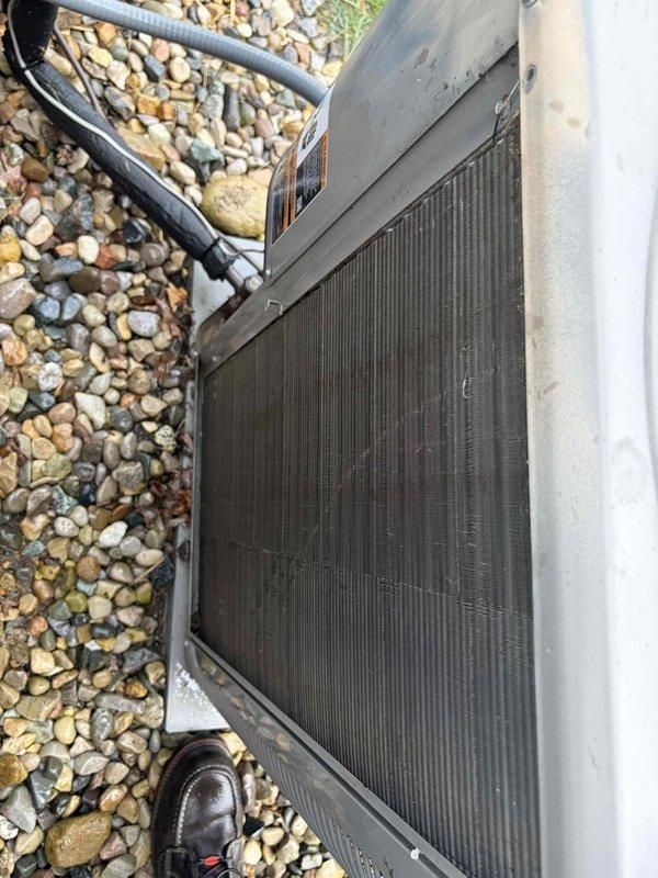 Performed preventative maintenance tune-up on residential air conditioning system. Inspected outdoor condenser unit, noting significant dirt and debris accumulation on heat exchanger coil fins requiring attention. Unit operational at time of service, with electrical connections and refrigerant lines secured properly at exterior wall junction.