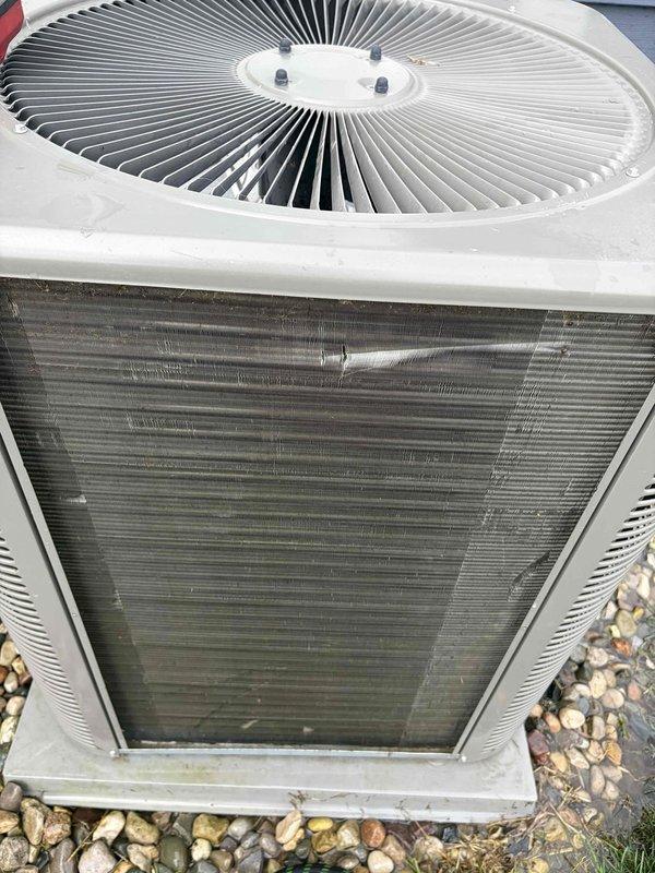 Performed preventative maintenance tune-up on residential air conditioning system. Inspected outdoor condenser unit, noting significant dirt and debris accumulation on heat exchanger coil fins requiring attention. Unit operational at time of service, with electrical connections and refrigerant lines secured properly at exterior wall junction.