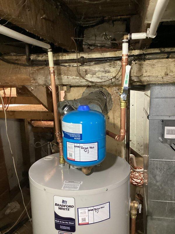 Removed and replaced water-damaged 40-gallon Bradford White natural gas water heater (Model N2S45S6FSR) in basement utility area following flooding event that compromised original unit. Installed new Bradford White water heater with proper copper piping connections, brass fittings, and blue expansion tank mounted on top of unit. Completed installation included pressure relief valve, proper venting for Category I natural draft appliance, and all connections to existing plumbing infrastructure mounted beneath wooden floor joists. Obtained necessary permit prior to installation and coordinated work alongside HVAC replacement crew to efficiently complete both systems affected by water damage.