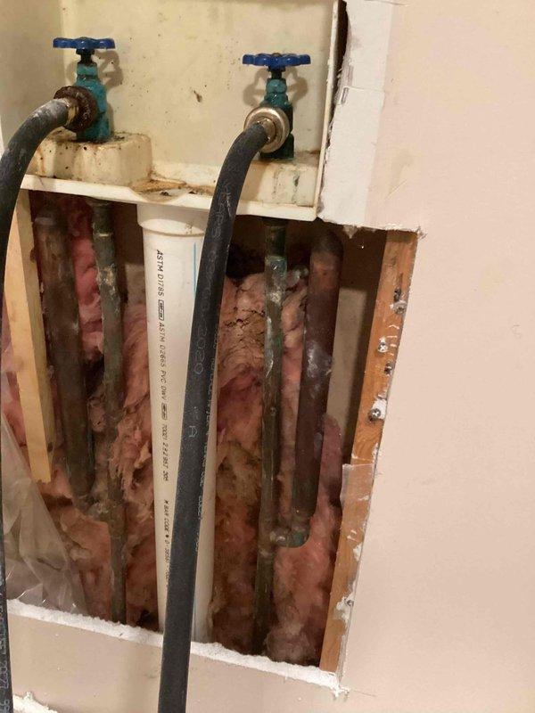 Responded to service call for corroded washing machine hookup faucets requiring replacement. Upon inspection, found significant corrosion and oxidation on copper supply lines and shut-off valves with deteriorated finish on hot and cold water connections. Removed section of drywall to access plumbing system behind washer box. Assessed extent of corrosion on copper piping throughout wall cavity. Replaced corroded washing machine shut-off valves with new hot and cold water supply valves. Installed new flexible supply hoses to washer box connections. Verified all connections for proper operation and absence of leaks. Documented existing plumbing conditions with photos showing before and during repair stages.