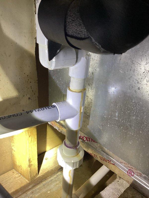 Responded to water leak at piping connection on water furnace in basement utility area. Upon inspection, identified slow drip at PVC condensate drain line assembly near furnace unit. Examined white PVC piping configuration including multiple 90-degree elbows, threaded couplings, and drain collection point with black grate cover. Assessed connection points and fittings for proper sealing and potential failure points. Noted moisture staining on concrete floor beneath affected area indicating previous leaking. Tightened connections at piping joints and verified all PVC fittings were properly secured. Inspected foam insulation on adjacent HVAC components for water damage. Tested system operation and monitored for active leaking. Confirmed leak was temporarily resolved and provided recommendations for ongoing monitoring. Documented equipment condition and piping assembly with photographs for service records.