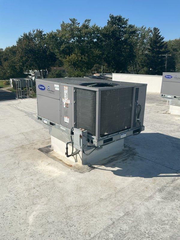 Successfully completed commercial rooftop unit installation at commercial facility. Installed new Carrier-branded RTU on properly positioned white concrete curb adapter on flat membrane roof. Unit secured to mounting pad with appropriate hardware and verified level installation for proper operation and drainage. Connected electrical conduit and completed all necessary electrical terminations per manufacturer specifications and local code requirements. Installed white PVC condensate drain line with proper pitch to ensure adequate drainage. Verified all manufacturer labels, warning stickers, and informational plates properly affixed to unit panels including "DO NOT BLOCK THIS END" warning label for proper airflow clearance. Confirmed adequate clearance around unit for service access and airflow requirements. Tested unit startup and verified proper operation of all components including compressor, condenser fan, and controls. System operating within normal parameters with no abnormalities