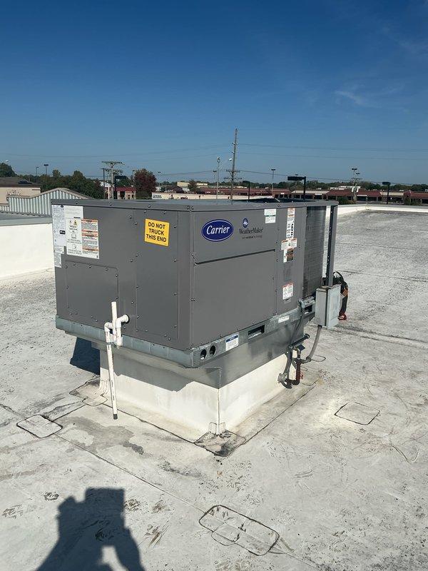Successfully completed commercial rooftop unit installation at commercial facility. Installed new Carrier-branded RTU on properly positioned white concrete curb adapter on flat membrane roof. Unit secured to mounting pad with appropriate hardware and verified level installation for proper operation and drainage. Connected electrical conduit and completed all necessary electrical terminations per manufacturer specifications and local code requirements. Installed white PVC condensate drain line with proper pitch to ensure adequate drainage. Verified all manufacturer labels, warning stickers, and informational plates properly affixed to unit panels including "DO NOT BLOCK THIS END" warning label for proper airflow clearance. Confirmed adequate clearance around unit for service access and airflow requirements. Tested unit startup and verified proper operation of all components including compressor, condenser fan, and controls. System operating within normal parameters with no abnormalities
