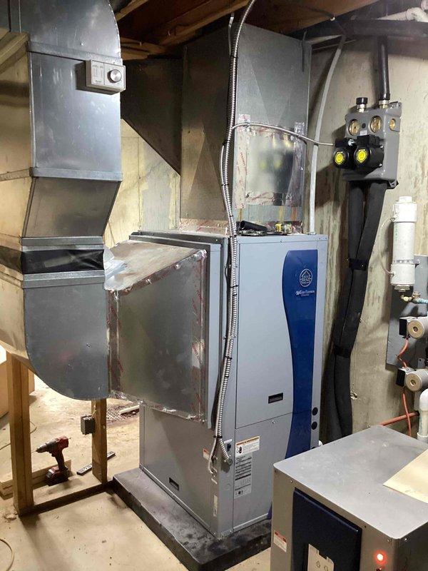 Installed a vertical geothermal water-source heat pump in the basement, connecting it to the supply and return ductwork with sealed, foil-taped transitions and mounting it on an isolation pad. Piped the ground loop through a manifold with isolation valves and insulated loop piping, with a filter/canister and condensate drain piping, then wired the line-voltage and control circuits, including the wall thermostat. Verified connections and completed system setup for operation.