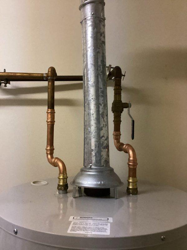 Installed a new 50-gallon gas tank-style water heater on the main floor, connecting copper supply lines with press-fit fittings, a brass ball valve on the cold inlet, and a galvanized flue vented through the draft hood. Replaced the home's main shutoff valve with a new brass valve and copper piping, restoring reliable whole-house water isolation. Verified connections are secure and leak-free, with no visible rust or moisture at the completed installation.