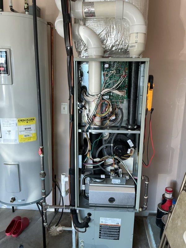 Performed a seasonal tune-up on a vertical gas furnace, removing the front access panel to inspect the control board, wiring, inducer blower motor, gas valve, and burner assembly. Verified electrical operation with a clamp meter and confirmed the PVC venting, flue connections, and gas piping were intact with no visible damage, corrosion, or leaks. The system was reassembled and left in proper working order.