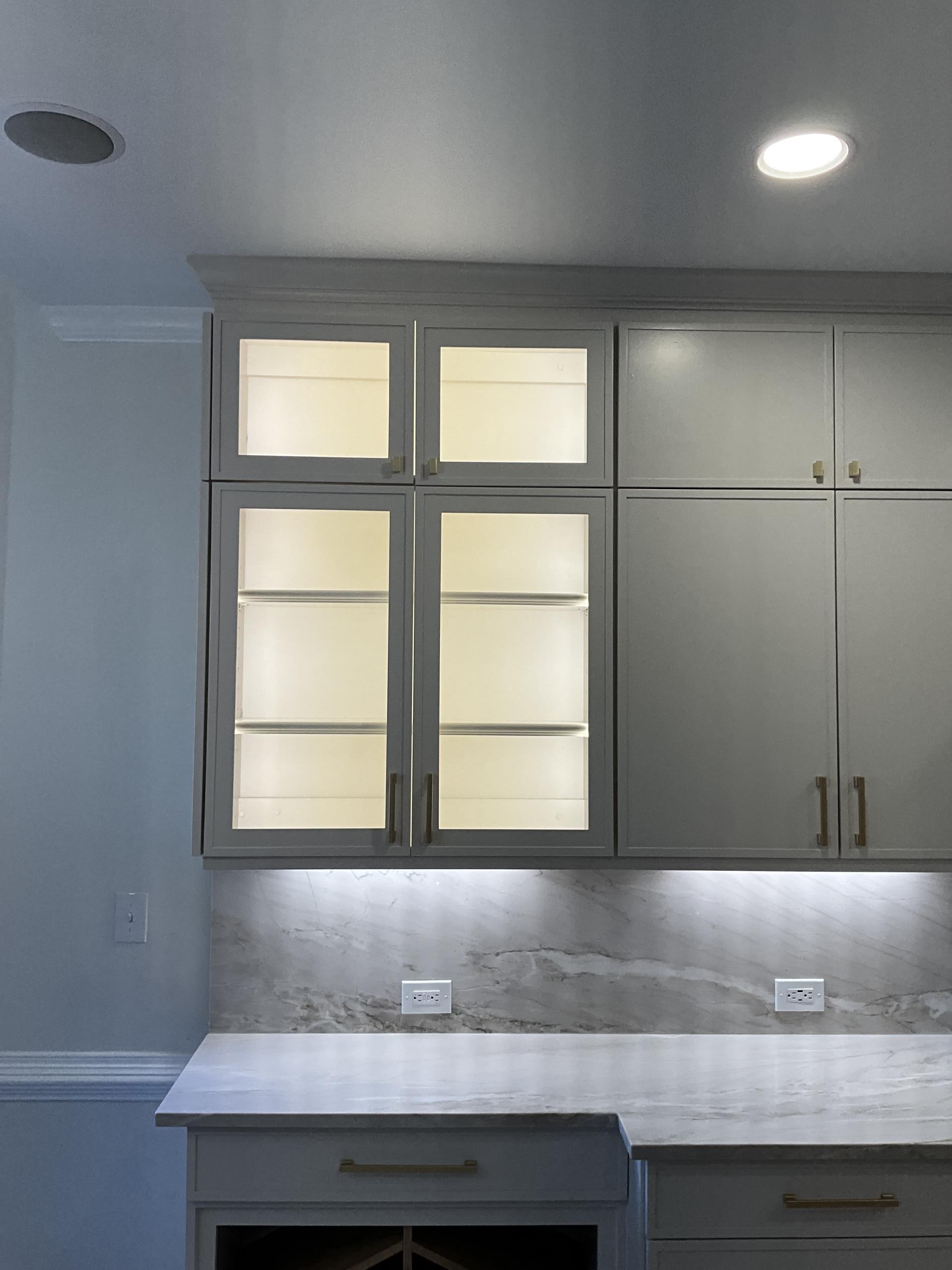I installed five white dimmable switches and relocated existing countertop receptacles from vertical to horizontal. Disposal wiring was moved to accommodate an air switch, and a dishwasher receptacle was added. Existing pendant lights were replaced with recessed canless can lights, and old can lights were swapped for new integrated LED versions. Five undercabinet lights were installed, along with a low voltage LED tape lighting system in cabinets and a new switch. Existing kitchen switches were moved to the opposite wall, and a single bronze receptacle was mounted on the island's end. A dedicated 20 amp circuit for the island microwave and a quad receptacle for the appliance garage were installed. New wiring was added to meet safety codes, including GFCI protection in the kitchen. Sheetrock removal was performed as needed.