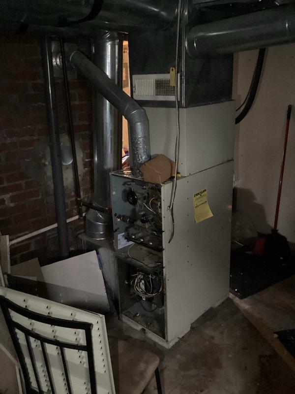 Conducted on-site assessment of aging furnace unit in basement utility room. System shows significant dust accumulation and wear on ductwork components. Noted exposed wiring on control unit with visible red, blue, and yellow wires. Prepared replacement estimate for customer to upgrade existing HVAC system with new energy-efficient equipment.