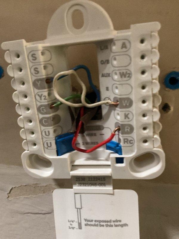 Conducted a replacement estimate for an aging HVAC system with visible exterior unit snow accumulation and deterioration. Inspected existing thermostat wiring configuration, noting multiple connections including Y, Y2, G, C, O/B, AUX, E, W, and R terminals with properly stripped wires. Exterior assessment revealed snow-covered heat pump/AC unit mounted against home's siding with existing electrical disconnect that will require replacement during system upgrade.