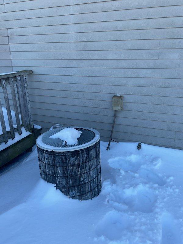 Conducted a replacement estimate for an aging HVAC system with visible exterior unit snow accumulation and deterioration. Inspected existing thermostat wiring configuration, noting multiple connections including Y, Y2, G, C, O/B, AUX, E, W, and R terminals with properly stripped wires. Exterior assessment revealed snow-covered heat pump/AC unit mounted against home's siding with existing electrical disconnect that will require replacement during system upgrade.