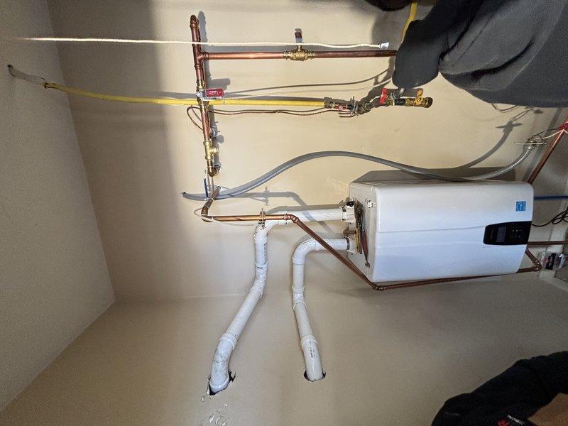 Successfully installed a GREENTankless water heater system with water softener for customer Brad CC. Installation included mounting the tankless unit on the wall, connecting copper supply lines with appropriate valves, installing PVC drain piping, and connecting the yellow gas line. All connections were properly secured and the system was tested for proper operation.