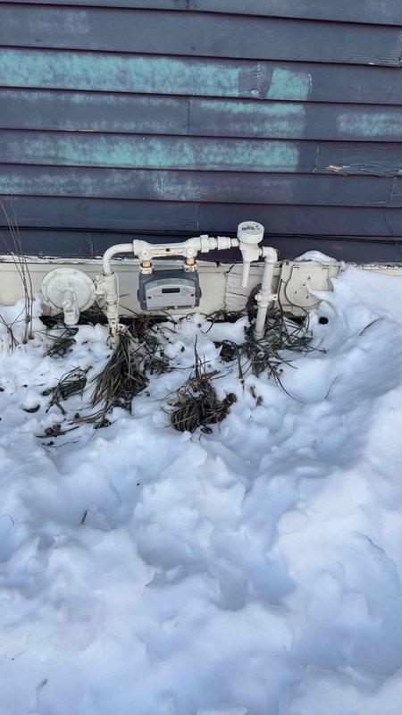 Conducted replacement estimate for non-functional boiler system in 5000 sq ft residence. Inspected existing equipment including aging blue boiler unit with metal exhaust ductwork and adjacent water heater. Noted exterior natural gas meter installation with PVC piping showing exposure to winter elements and weathered building exterior. Discussed potential replacement options and repair alternatives with homeowner.