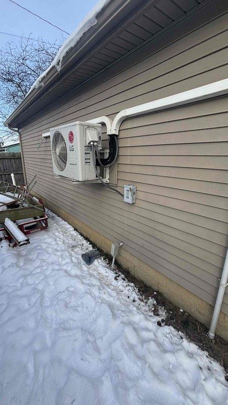 Conducted exterior assessment of existing LG heat pump system during winter conditions. Documented current installation configuration including refrigerant line routing, PVC condensate drainage, and wall penetration. Evaluated equipment for potential replacement, noting current placement considerations and existing line set pathways through vinyl siding exterior.