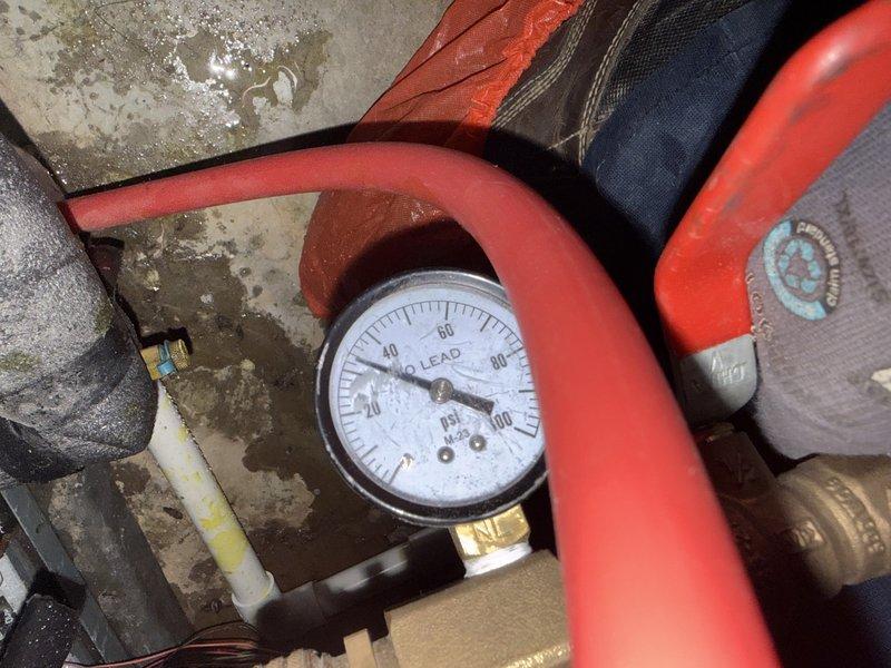 Investigated customer complaint of "battery acid" smell originating from area above heat pump in basement. Conducted pressure testing on system, with gauge readings showing approximately 20 psi. No refrigerant leaks detected that would explain the reported odor.