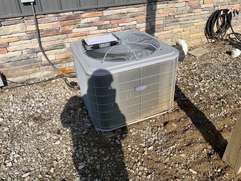 Conducted comprehensive assessment of existing outdoor HVAC condensing unit installed on gravel bed adjacent to stone veneer exterior wall. Unit appears to have standard electrical disconnect box mounted on metal post with proper connections to building. Evaluated system for potential replacement options as requested by homeowner Jeremy, with both Jeremy and Jake present during the consultation.