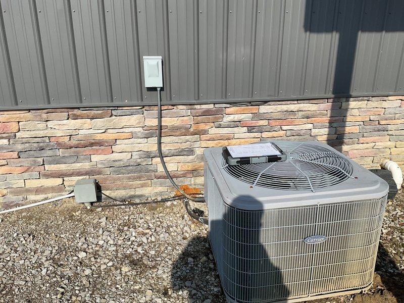 Conducted comprehensive assessment of existing outdoor HVAC condensing unit installed on gravel bed adjacent to stone veneer exterior wall. Unit appears to have standard electrical disconnect box mounted on metal post with proper connections to building. Evaluated system for potential replacement options as requested by homeowner Jeremy, with both Jeremy and Jake present during the consultation.