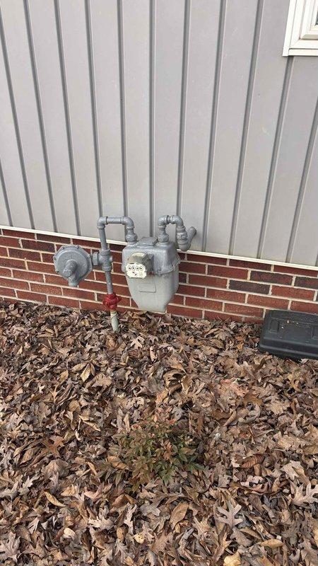 Conducted comprehensive HVAC replacement assessment at residential property, documenting existing natural gas meter installation mounted on brick foundation with vertical siding. Photographed and evaluated current gas service configuration including meter assembly, regulator valve, and shutoff mechanisms to determine compatibility with proposed new HVAC system.