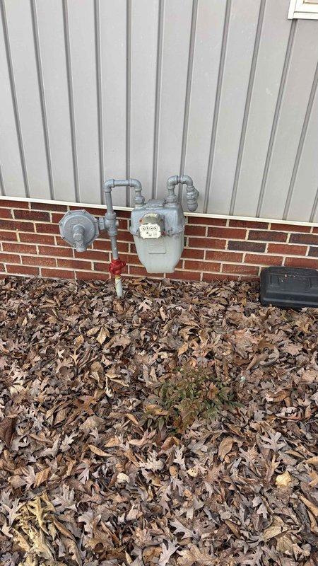 Conducted comprehensive HVAC replacement assessment at residential property, documenting existing natural gas meter installation mounted on brick foundation with vertical siding. Photographed and evaluated current gas service configuration including meter assembly, regulator valve, and shutoff mechanisms to determine compatibility with proposed new HVAC system.