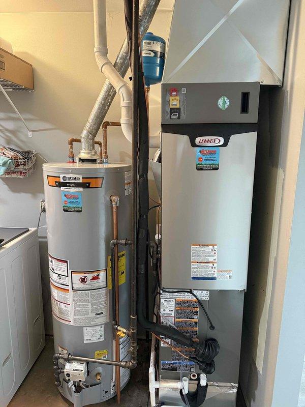 Successfully installed a complete Lennox HVAC system with outdoor condenser unit mounted on concrete pad against brick exterior wall, including proper electrical connections and refrigerant lines. Indoor air handler was installed in utility room alongside existing State water heater, with all necessary ductwork, PVC venting, and electrical components properly connected. System was tested and verified to be functioning according to manufacturer specifications.