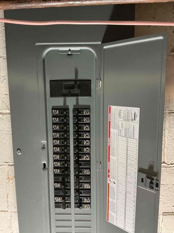 Completed panel replacement service (WO #15958), replacing outdated electrical panel with new circuit breaker panel featuring dual columns of properly labeled circuit breakers. Installation included proper mounting to concrete block wall with main breaker switch and comprehensive circuit directory for improved safety and functionality.