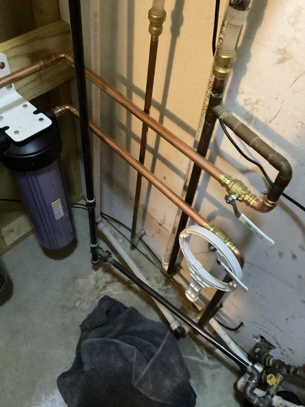 Successfully installed a comprehensive whole-house water filtration system consisting of dual black cylindrical filter housings with white bracket supports securely mounted to the wall structure. Connected the system to existing copper plumbing infrastructure using brass fittings and valves, ensuring proper integration with the home's water supply network including PEX connections where appropriate.