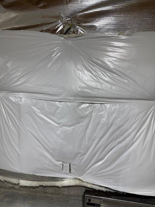 Inspected interior wall with vapor barrier installation where plastic sheeting had been properly cut around electrical outlets. Verified that the electrical receptacle was accessible through the moisture barrier and confirmed the junction box remained properly secured. Noted the vapor barrier installation was suitable for continued electrical service in what appears to be an unfinished space.