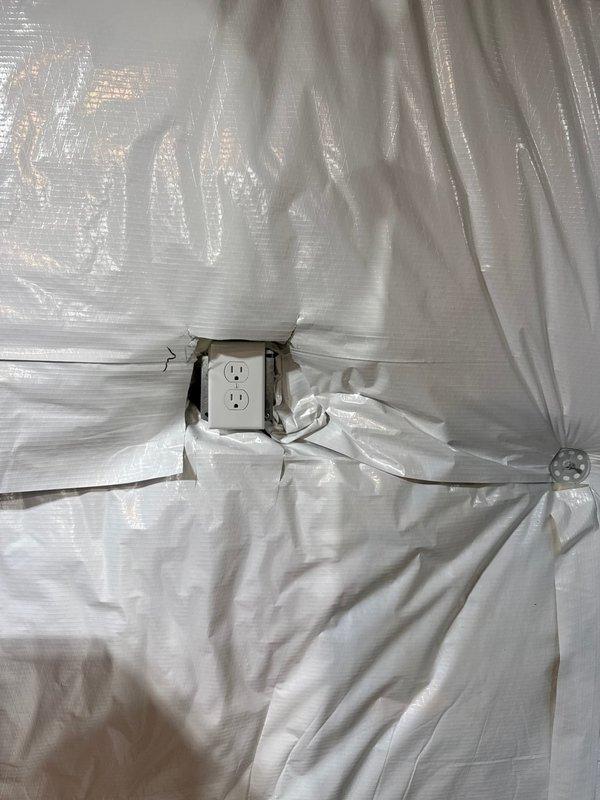 Inspected interior wall with vapor barrier installation where plastic sheeting had been properly cut around electrical outlets. Verified that the electrical receptacle was accessible through the moisture barrier and confirmed the junction box remained properly secured. Noted the vapor barrier installation was suitable for continued electrical service in what appears to be an unfinished space.