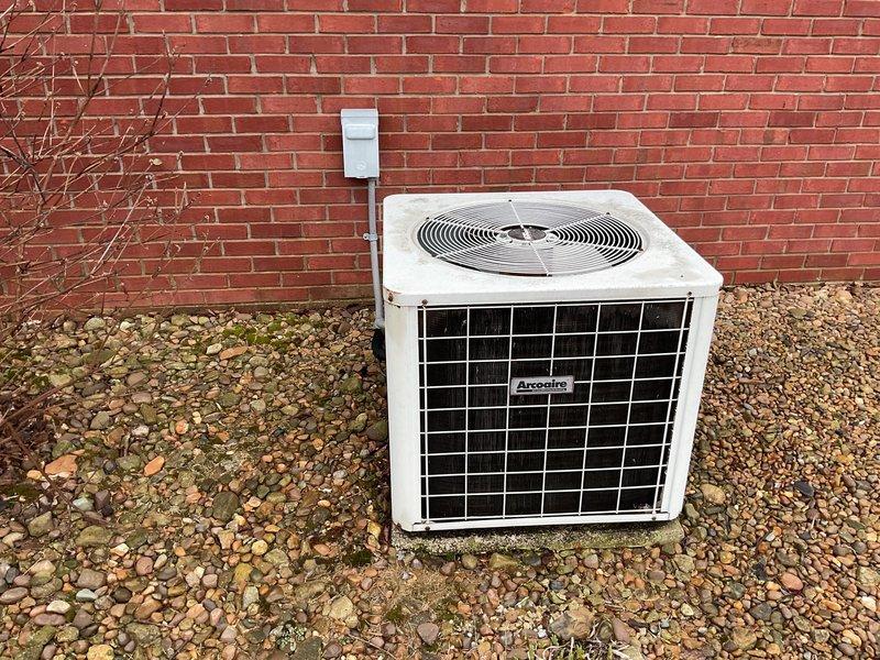 Conducted a comprehensive replacement estimate for converting an aging Arcoaire HVAC system to natural gas. Inspection revealed weathered outdoor AC unit installed on gravel base with visible weathering and discoloration. Interior mechanical room houses current water heater and HVAC equipment on partially finished flooring (transition between hardwood and OSB subflooring), indicating potential space considerations for new system installation.