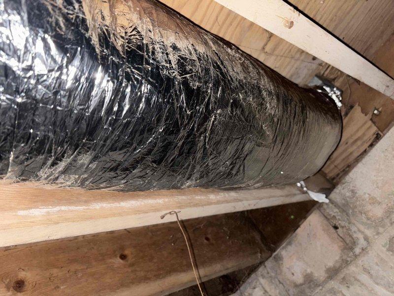 Performed follow-up inspection of previously repaired ductwork to address insufficient airflow in living room vent. Examined black insulated flexible ducts in crawl space, noting areas of damaged insulation with protruding fiberglass fibers. Identified restriction in airflow causing cool air delivery despite previous repair work.