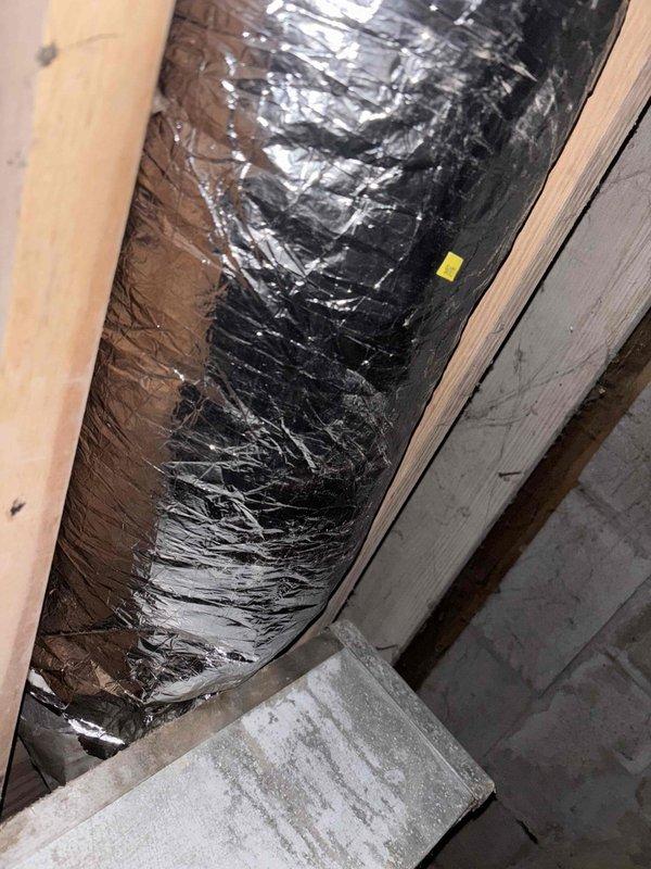 Performed follow-up inspection of previously repaired ductwork to address insufficient airflow in living room vent. Examined black insulated flexible ducts in crawl space, noting areas of damaged insulation with protruding fiberglass fibers. Identified restriction in airflow causing cool air delivery despite previous repair work.