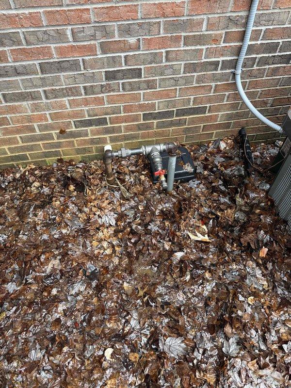 Completed installation of gas lines per sales agreement. Work included mounting a plumbing assembly with T-junction and shut-off valve on wooden baseboard, and installing exterior metal pipe configuration with red valve handle at the brick wall perimeter. All connections were properly secured and tested for functionality.