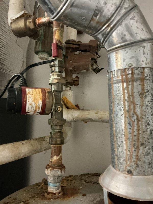 Performed site visit to inspect recertification pump system. Documented existing water heater installation showing signs of wear including damaged pipe insulation and corrosion on copper pipes and fittings. Noted significant oxidation on plumbing components, particularly at joints, with visible rust streaks on galvanized metal ductwork requiring attention during recertification process.