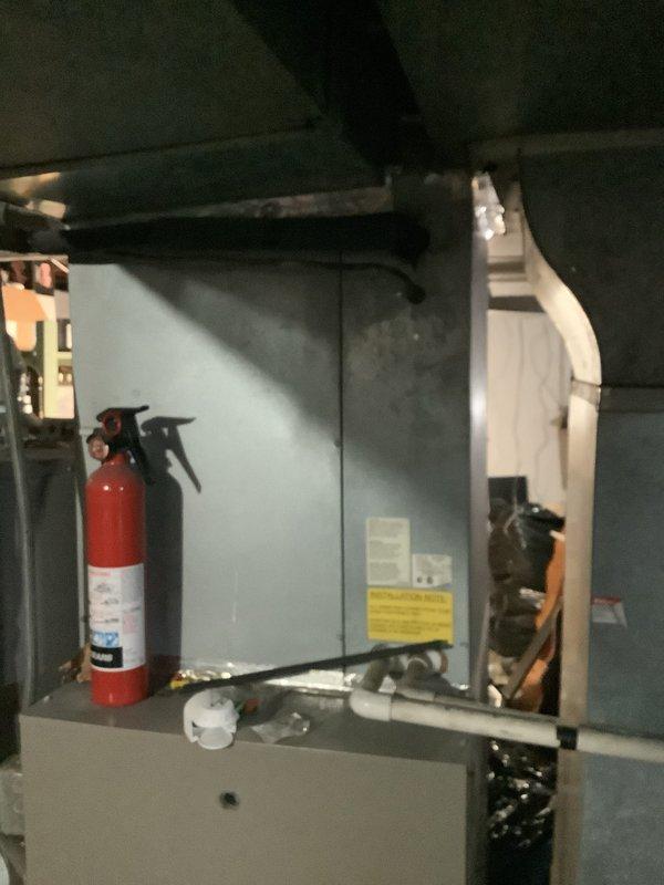 Conducted replacement estimate for 20-year-old non-functioning HVAC system. Inspection revealed aging indoor furnace unit with attached documentation in utility area, alongside fire safety equipment. Exterior assessment showed weathered condenser unit with visible deterioration, installed against brick wall with significant algae growth and poor surrounding maintenance.