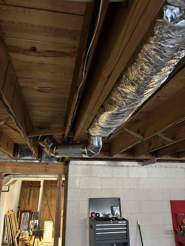Conducted follow-up site visit to evaluate bathroom register relocation requirements following customer remodel. Inspected existing HVAC ductwork in unfinished basement area, noting cylindrical ducts with reflective metallic insulation and elbow joint connections. Documented current installation with photographs for proper planning of register repositioning work.