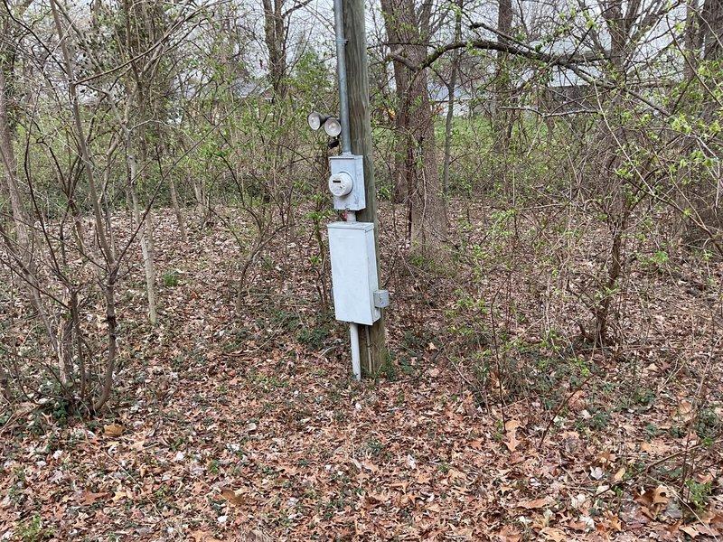 Completed site assessment for whole home generator installation. Documented existing electrical service panel mounted outdoors in wooded area showing signs of weathering with vegetation growth nearby. Evaluated utility pole installation with meter connection to determine appropriate generator sizing and placement options for future whole home backup power system.
