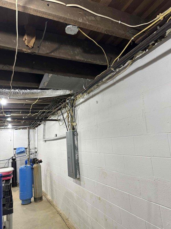Conducted follow-up inspection of unfinished basement area with exposed ceiling joists to assess incomplete gas line installation work. Documented existing utility infrastructure including electrical panel, water pressure tank, and filtration system. Observed partially removed ceiling panels revealing metal framing elements and electrical wiring that will require consideration during gas line completion.
