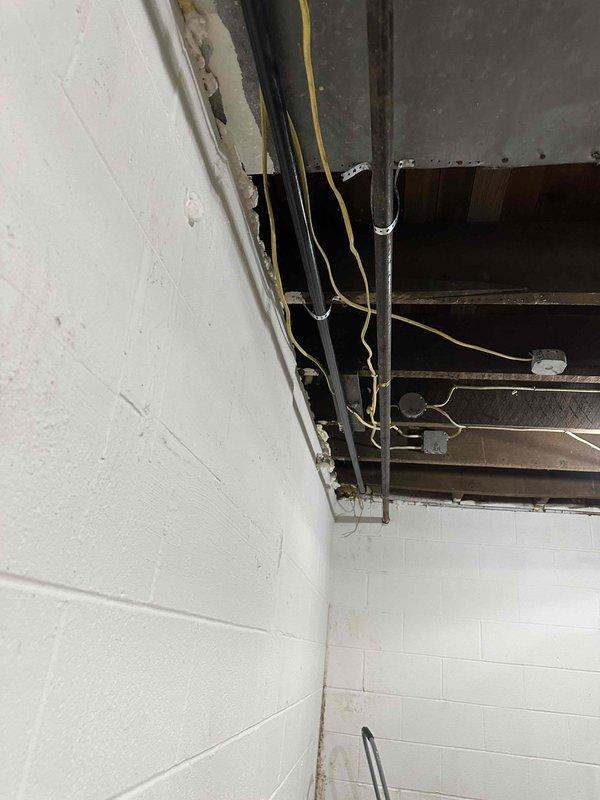 Conducted follow-up inspection of unfinished basement area with exposed ceiling joists to assess incomplete gas line installation work. Documented existing utility infrastructure including electrical panel, water pressure tank, and filtration system. Observed partially removed ceiling panels revealing metal framing elements and electrical wiring that will require consideration during gas line completion.