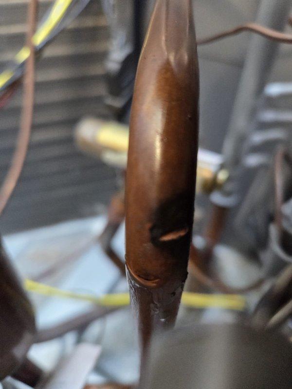 # HVAC Service Report

Responded to no-cooling complaint on 2-year-old AC system with ongoing temperature control issues since installation. Upon inspection, discovered catastrophic refrigerant leak caused by punctured copper suction line. Hole in copper tubing resulted in complete loss of refrigerant charge, preventing system from achieving desired cooling capacity below 79 degrees. Documented damage with photographs showing compromised copper pipe and thermal expansion valve assembly. Leak represents manufacturing defect or installation damage that has progressively worsened over the two-year service period, explaining the chronic underperformance and previous unsuccessful repair attempts.